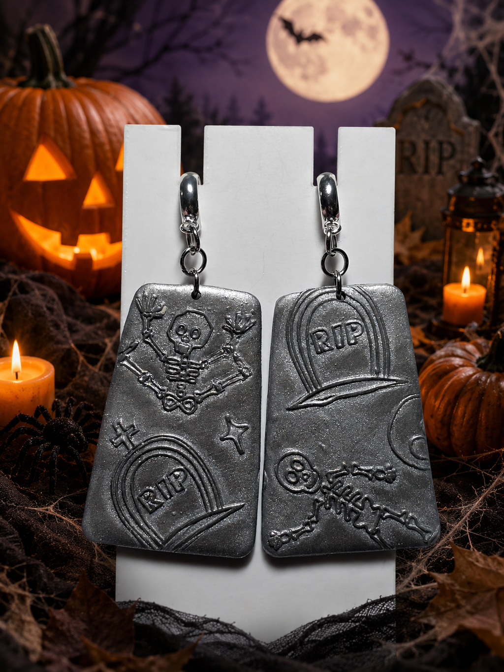 Silver polymer clay dangle earrings with embossed Halloween graveyard scene including skeleton, RIP tombstones, crescent moon and stars